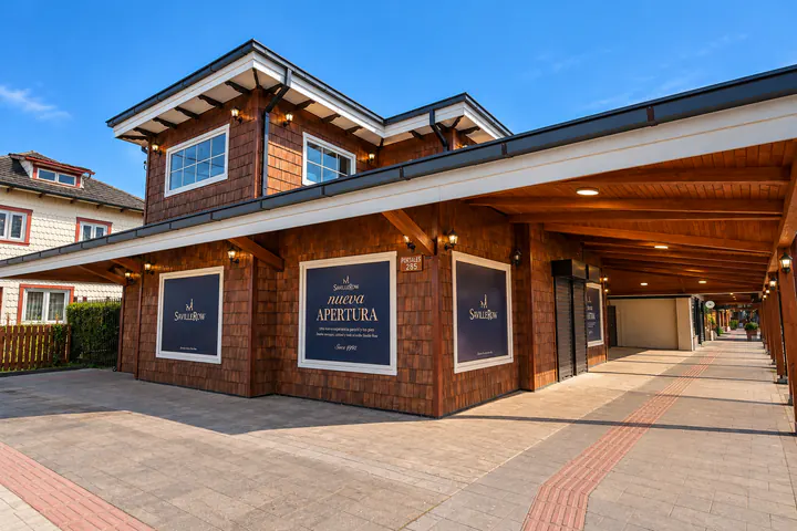 Casa Kauak: local esquina revestido en tejuela bajo un portal de madera, con las vitrinas de la nueva tienda de Saville Row, a plena luz del día.