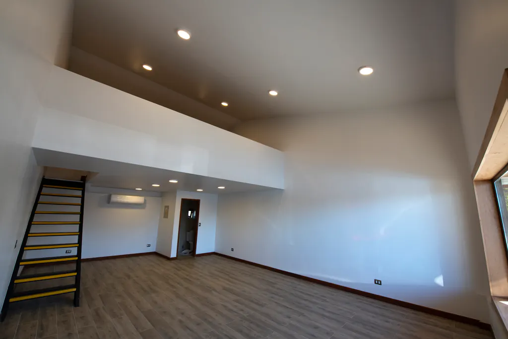 Local de dos niveles recién terminado, con piso de madera, muros blancos y una escalera al entrepiso.